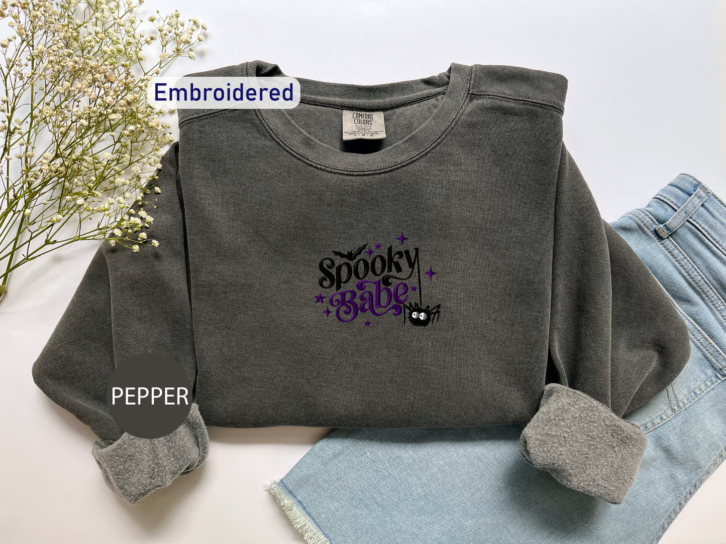 a gray sweatshirt with spooky stuff on it next to a pair of jeans