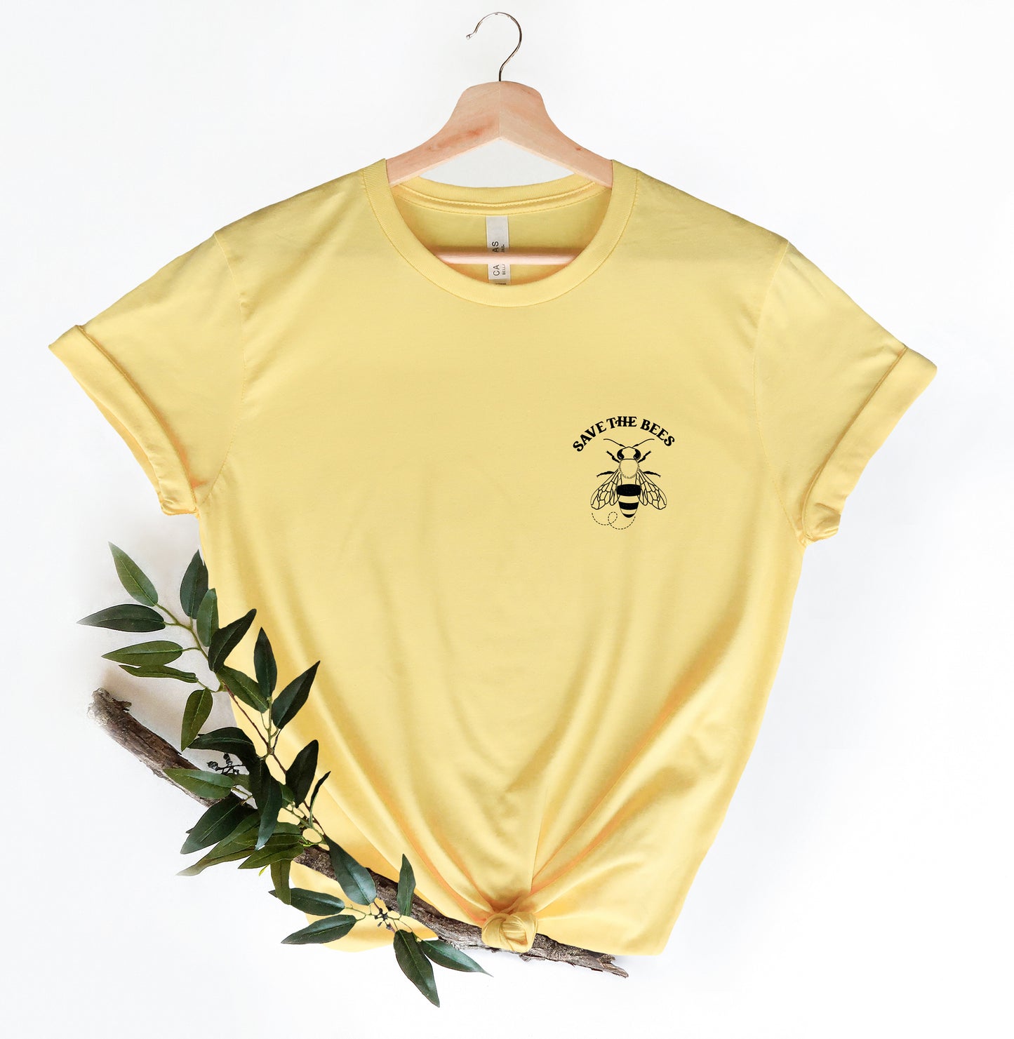 A yellow t-shirt with a graphic of a bee and the text "SAVE THE BEES" printed on it, hanging on a wooden hanger.
