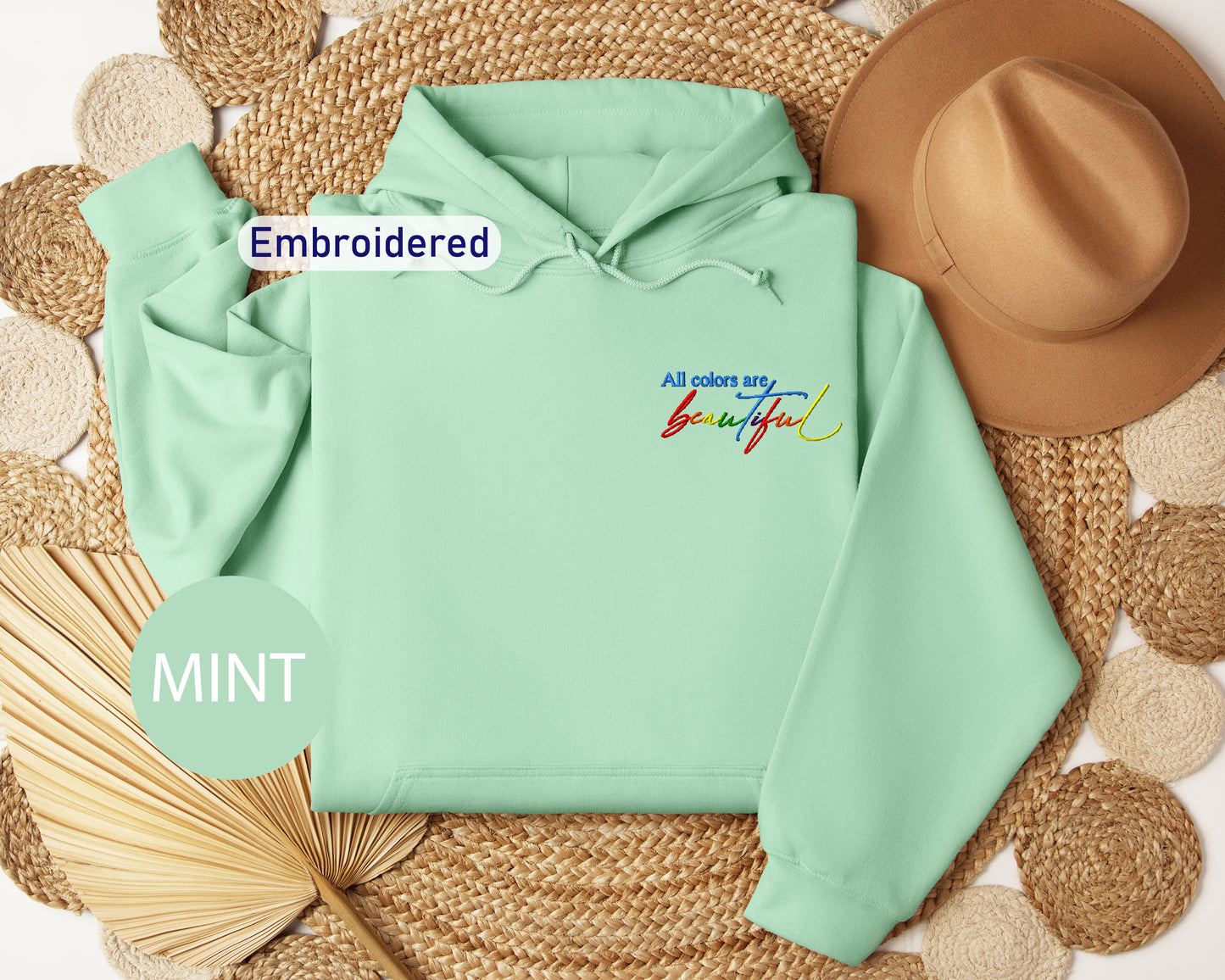 a mint green hoodie with embroidered words and a straw hat