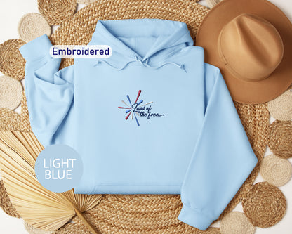 a light blue hoodie with a patriotic design, a brown hat, and a straw hat, all arranged on a woven mat.