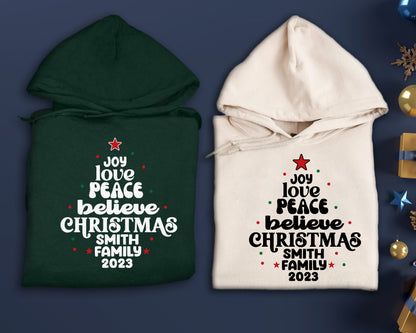 two hooded sweatshirts with Christmas-themed text printed on them, placed on a blue background.