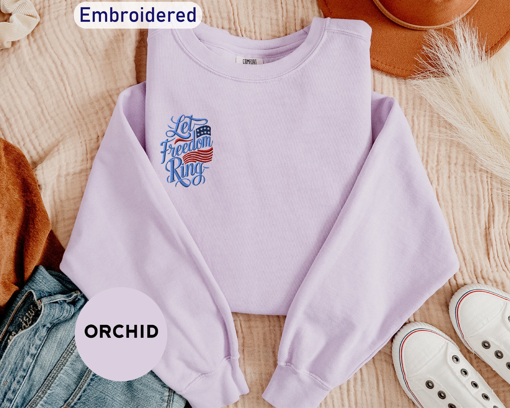 a purple sweatshirt with an embroidered design, a pair of jeans, a hat, and a pair of white sneakers, all laid out on a surface.