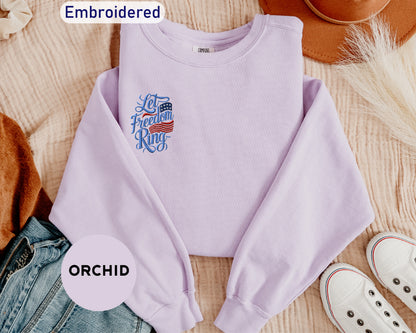 a purple sweatshirt with an embroidered design, a pair of jeans, a hat, and a pair of white sneakers, all laid out on a surface.
