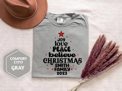a gray t-shirt with a Christmas tree design, a brown hat, and some dried flowers, all arranged on a white background.