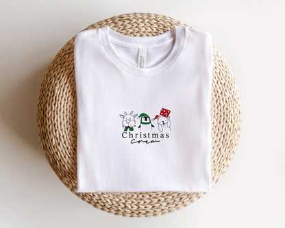 A white t-shirt with a Christmas-themed graphic design printed on it, placed on a woven basket.