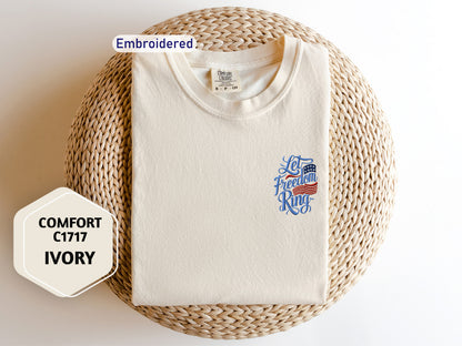 a white t-shirt with a patriotic design, laid out on a woven basket. The t-shirt has a label on the collar and a sticker on the front. There is also a hexagonal sticker with text next to the t-shirt.