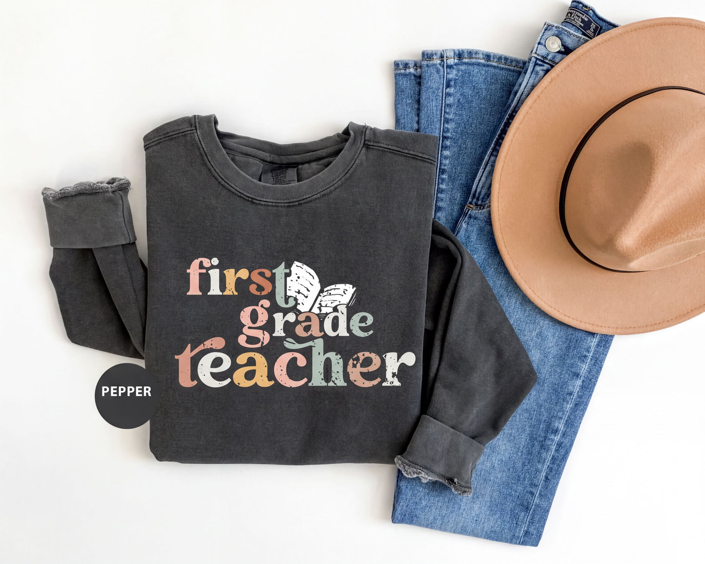 A black sweatshirt with the text "first grade teacher" printed on it, along with a pair of blue jeans and a tan hat.