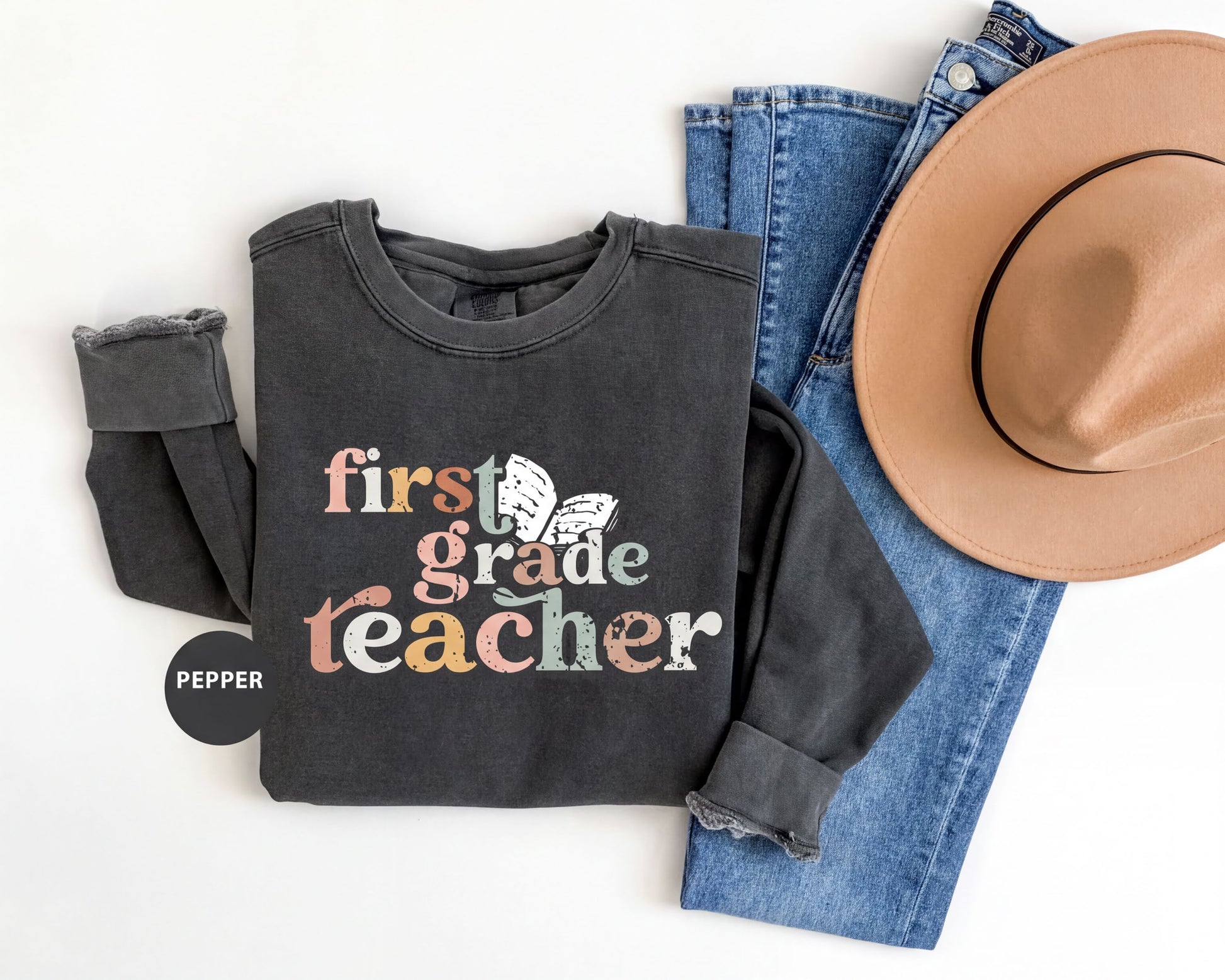 A black sweatshirt with the text "first grade teacher" printed on it, along with a pair of blue jeans and a tan hat.
