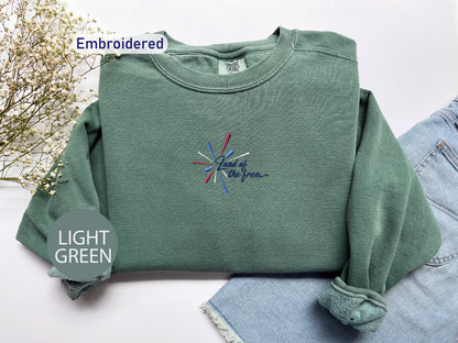 a green sweatshirt with a colorful embroidered design on it, placed on a white surface alongside a pair of denim jeans.