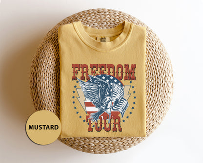 A yellow t-shirt with a graphic design featuring an eagle and the words "FREEDOM TOUR" printed on it, placed on a woven basket.