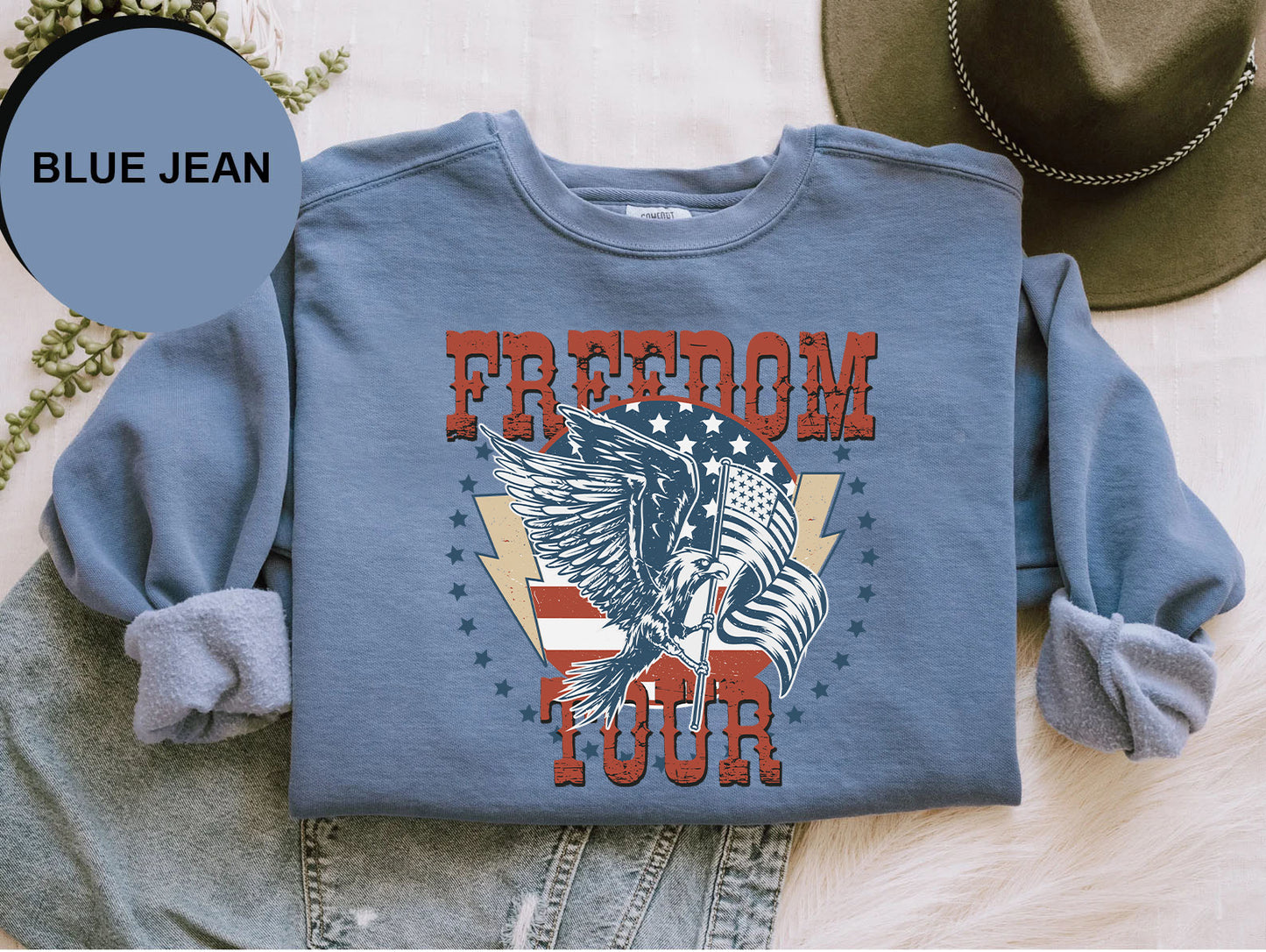 A blue sweatshirt with a graphic design featuring a large eagle and the text "FREEDOM TOUR" printed on it, along with a hat and some jeans.