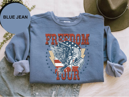 A blue sweatshirt with a graphic design featuring a large eagle and the text "FREEDOM TOUR" printed on it, along with a hat and some jeans.