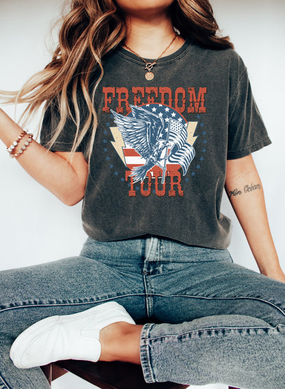 A woman wearing a black t-shirt with a graphic design and the text "FREEDOM TOUR" is sitting on a chair.