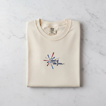 A cream-colored t-shirt with a graphic design and text printed on it, laid out on a marble surface.