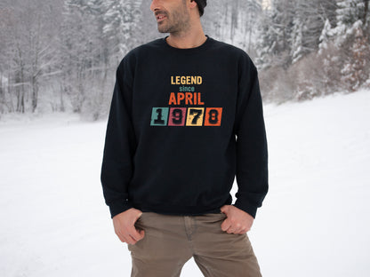 A man wearing a black sweatshirt with the text "LEGEND since APRIL 1978" printed on it, standing in a snowy forest.