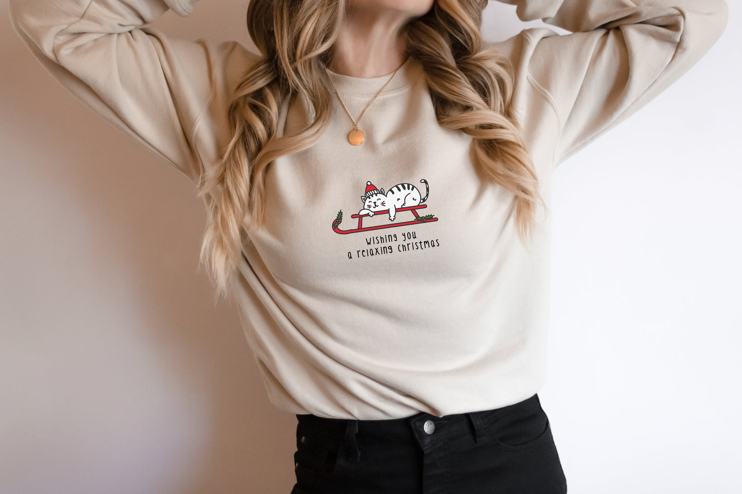 A woman wearing a white sweater with a graphic of a cat on a sled and text that says "Wishing you a happy xmas"