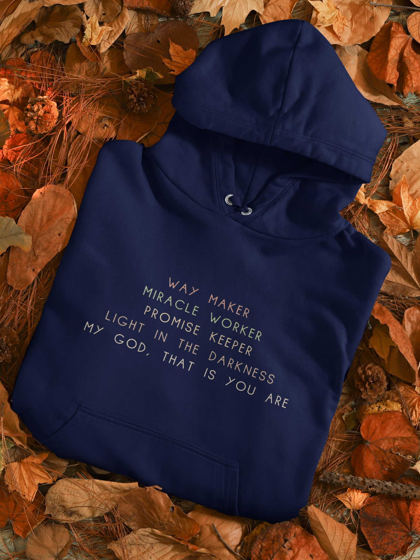 A navy blue hoodie with white text printed on it, laying on a bed of autumn leaves.