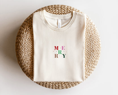 A white t-shirt with the word "MERRY" printed on it, laid out on a woven basket or mat.