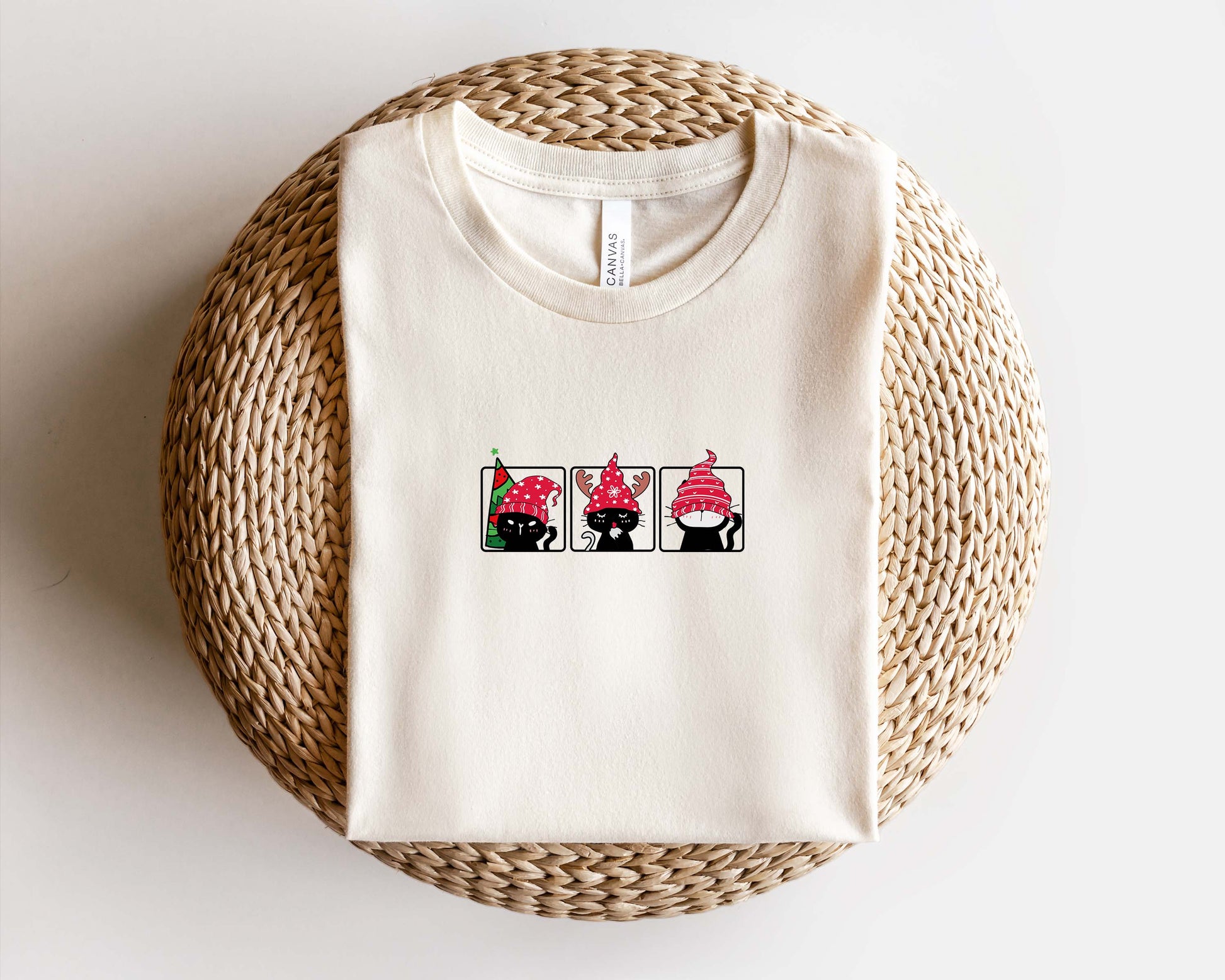 A white t-shirt with a graphic design of three cats wearing red hats, arranged in a row.