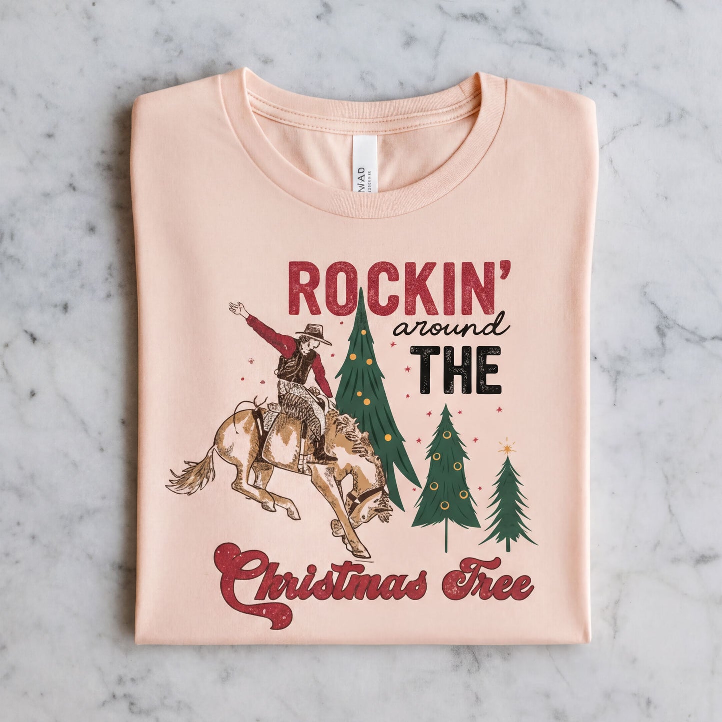 A t-shirt with a graphic design depicting a cowboy riding a bucking bronco, with Christmas trees and the text "ROCKIN' around THE CHRISTMAS Tree" printed on it.