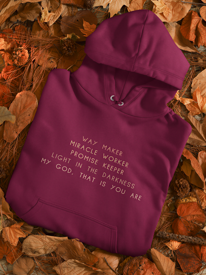 A maroon hoodie with white text is laid out on a bed of autumn leaves.