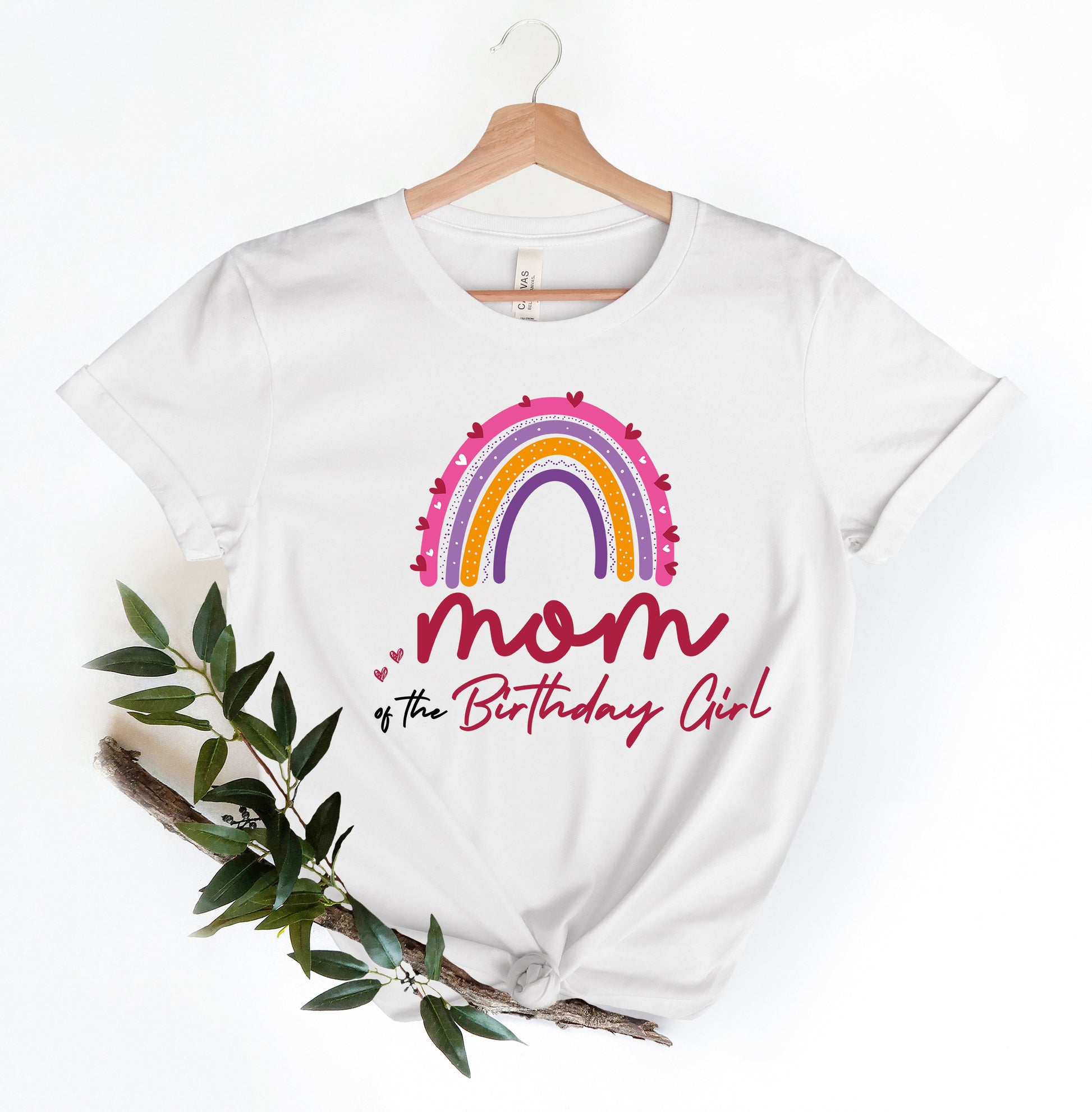 A white t-shirt with a colorful graphic design and text printed on it, hanging on a wooden hanger.