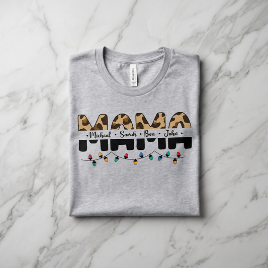 A gray t-shirt with a graphic design featuring the word "MAMA" in a leopard print font, along with the names "Michael", "Sarah", and "Ben" written below it. The design also includes colorful Christmas lights.