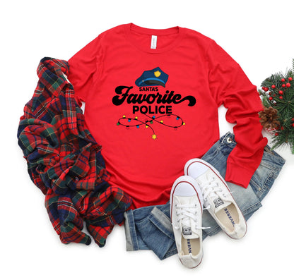 A red long-sleeved shirt with a Santa hat and the text "Santa's Favorite Police" printed on it, along with a pair of jeans and white sneakers, are laid out on a white background.