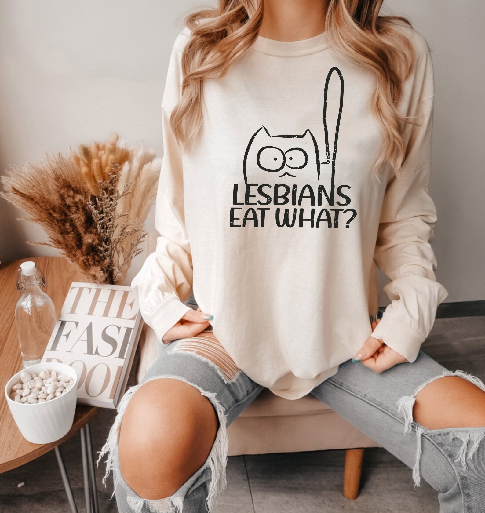 a woman sitting on a couch wearing a sweatshirt that says lesbians eat what?