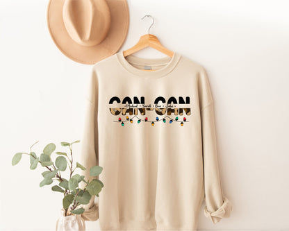 A beige sweatshirt with the text "CAN CAN" printed on it, along with a cowboy hat and a plant in a white vase, all displayed on a wooden hanger against a white wall.