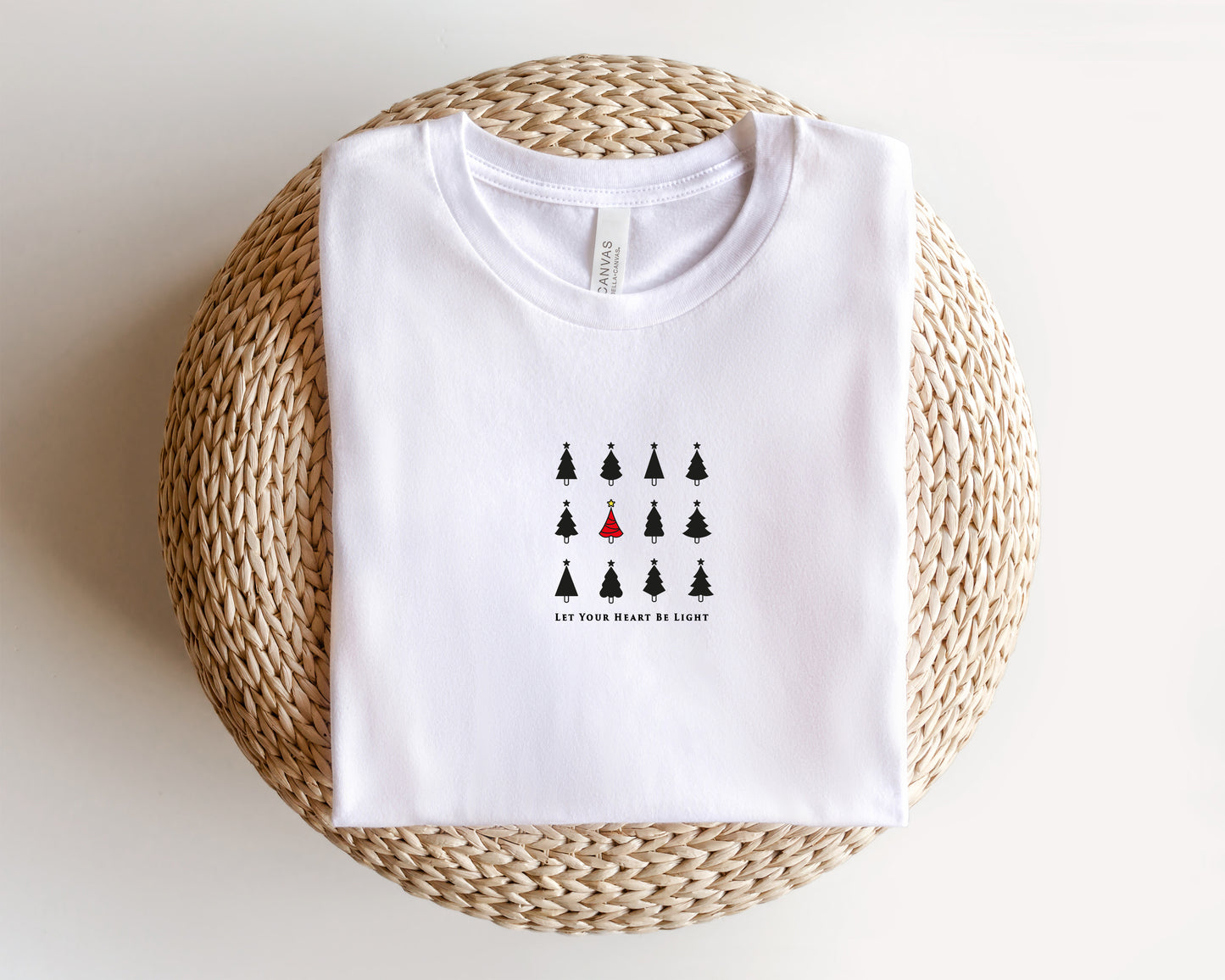 A white t-shirt with a graphic design of a group of black Christmas trees and the text "Let your heart be light" printed on it.