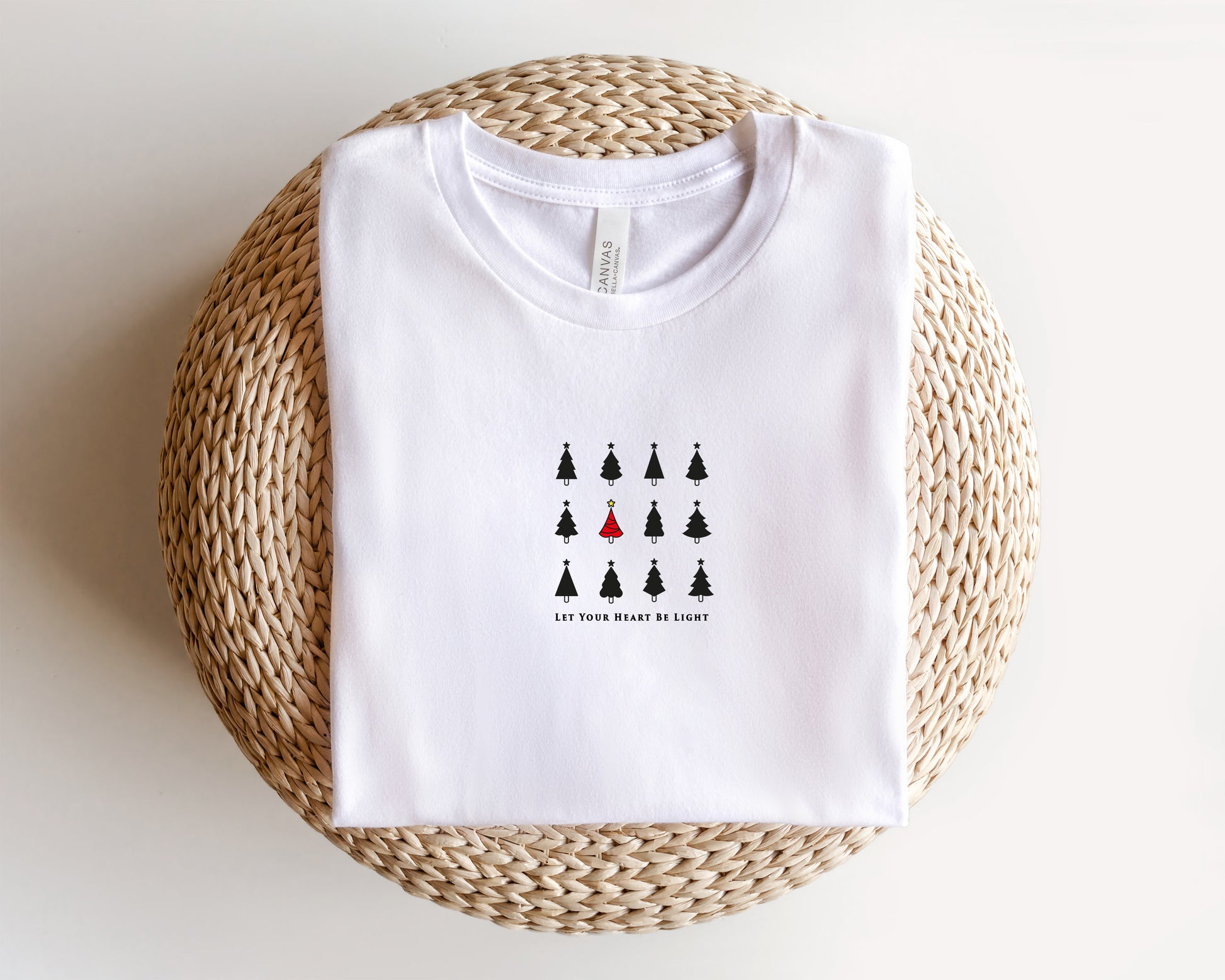 A white t-shirt with a graphic design of a group of black Christmas trees and the text "Let your heart be light" printed on it.
