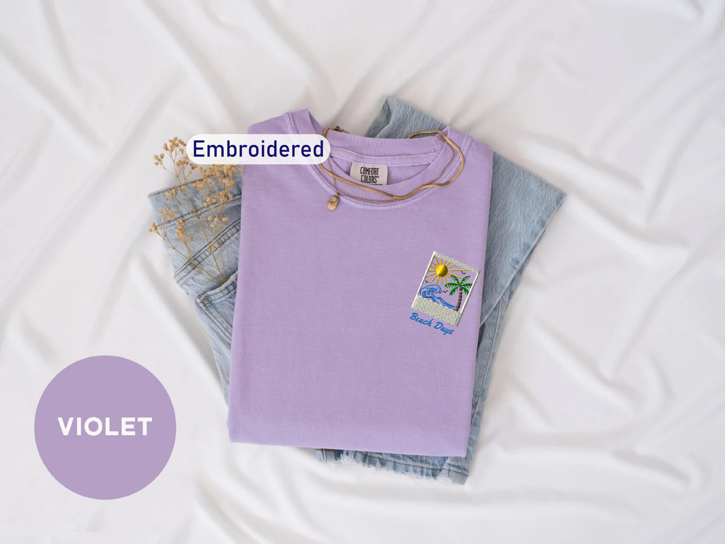 a purple t-shirt with a beach-themed design, a pair of denim jeans, and a small embroidered patch on the t-shirt. The text "Embroidered" is visible, indicating that the t-shirt has been embroidered.