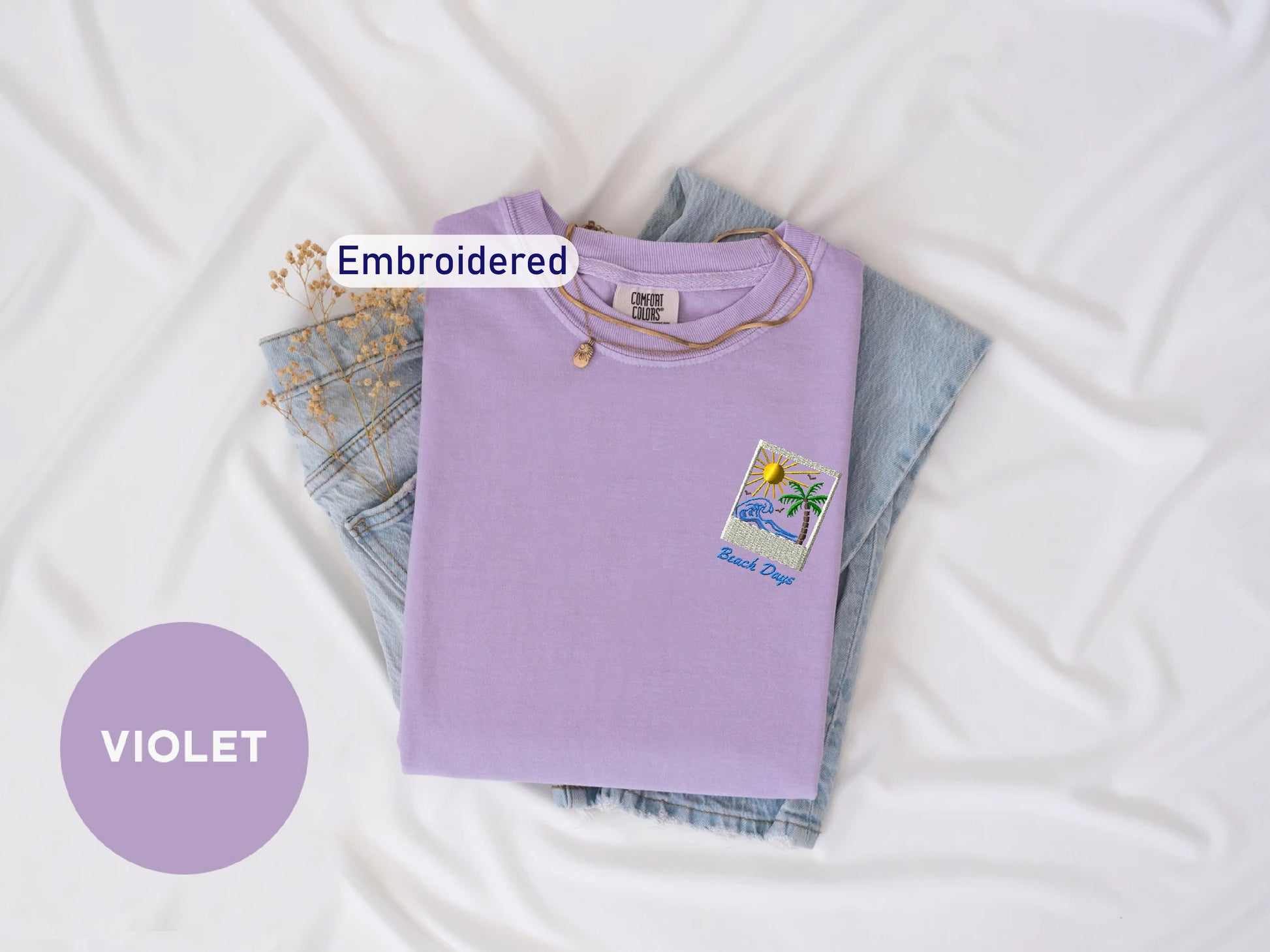 a purple t-shirt with a beach-themed design, a pair of denim jeans, and a small embroidered patch on the t-shirt. The text "Embroidered" is visible, indicating that the t-shirt has been embroidered.