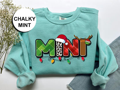 A turquoise sweatshirt with a graphic design featuring the word "MINI" in a colorful, festive font, along with a Santa hat and antlers.