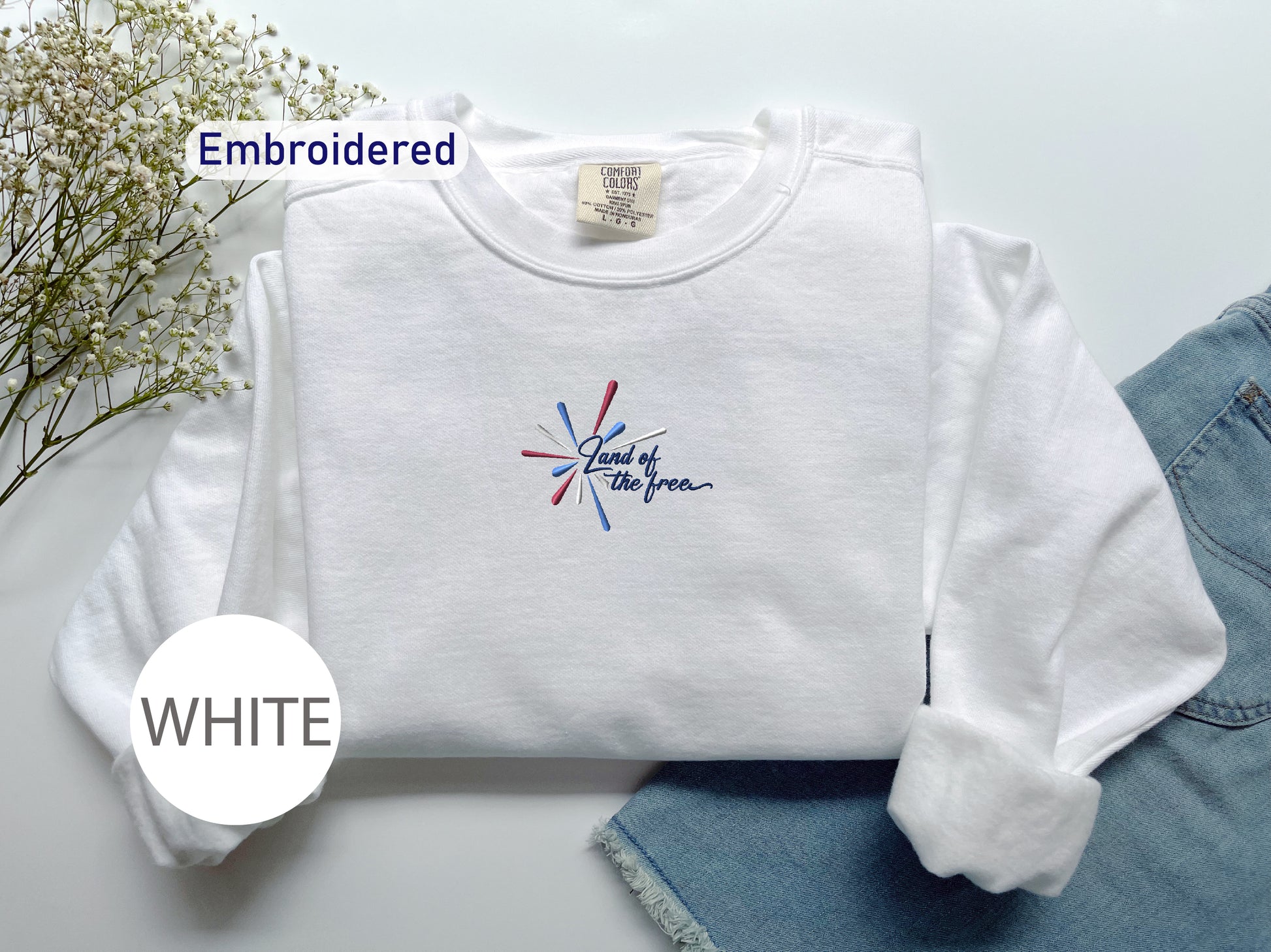 a white long-sleeved shirt with a patriotic design, a pair of blue jeans, and some flowers on a white background.