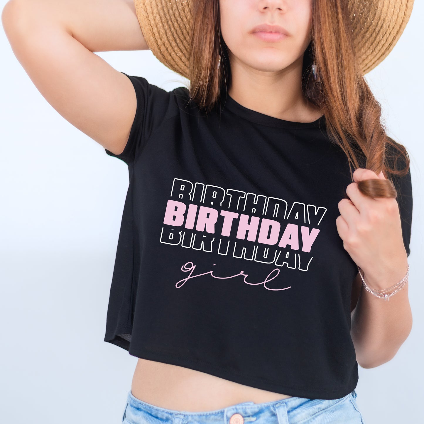 A woman wearing a black crop top with the text "BIRTHDAY girl" printed on it, along with a straw hat.
