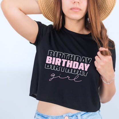 A woman wearing a black crop top with the text "BIRTHDAY girl" printed on it, along with a straw hat.