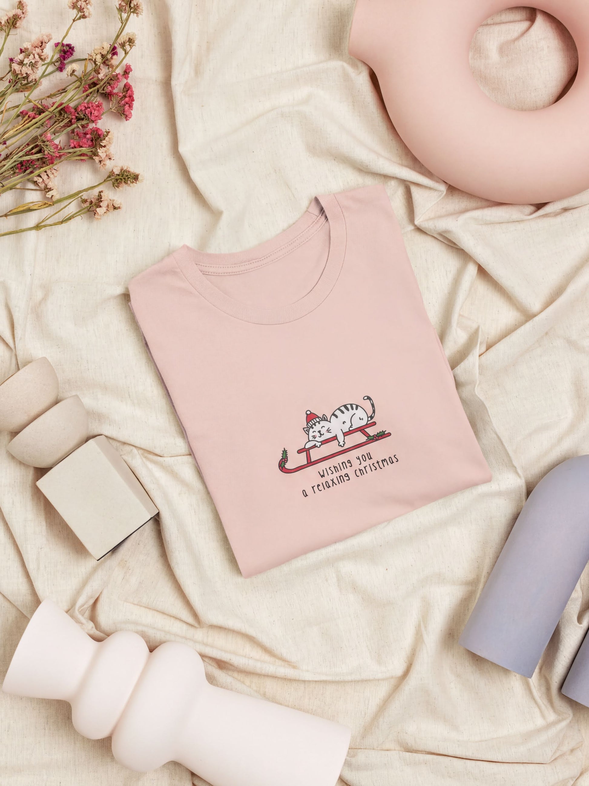 a pink t-shirt with a cat graphic and text, along with some other items such as a vase, a teapot, and a pink ceramic object.