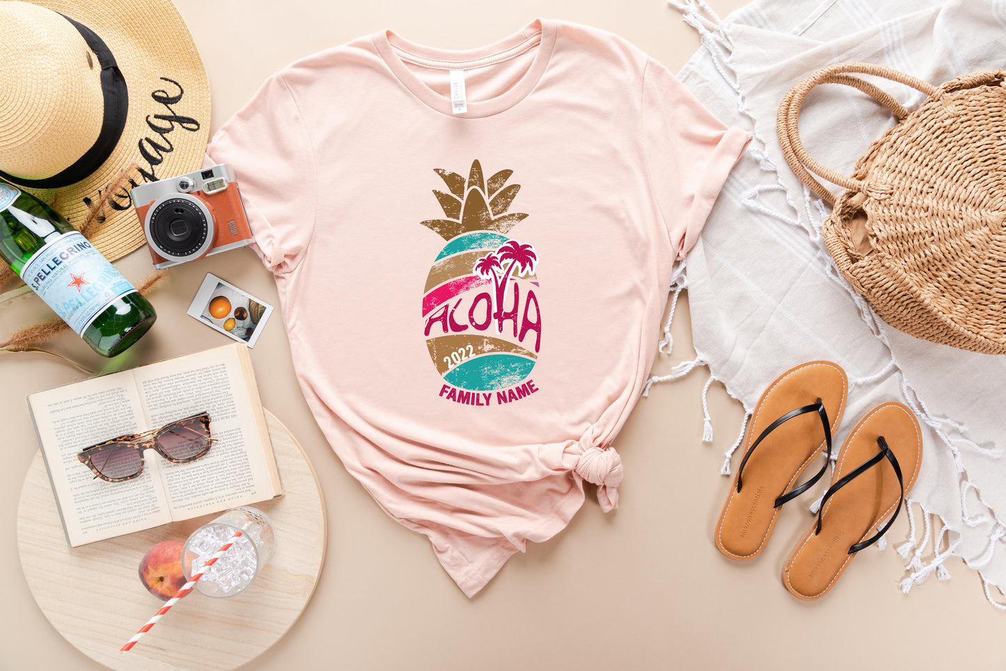 a casual arrangement of summer-themed items, including a pink t-shirt with a pineapple graphic, sunglasses, a straw, a hat, a book, a bottle, a cup, and a pair of flip-flops.