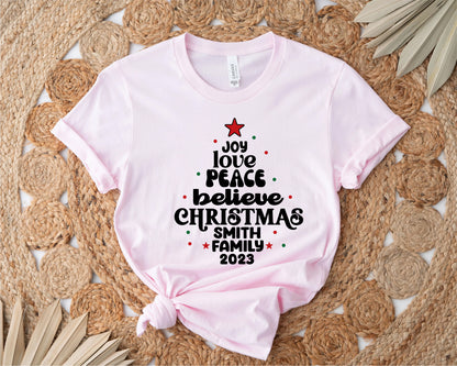 A pink t-shirt with a Christmas-themed design printed on it, placed on a woven mat with palm leaves.