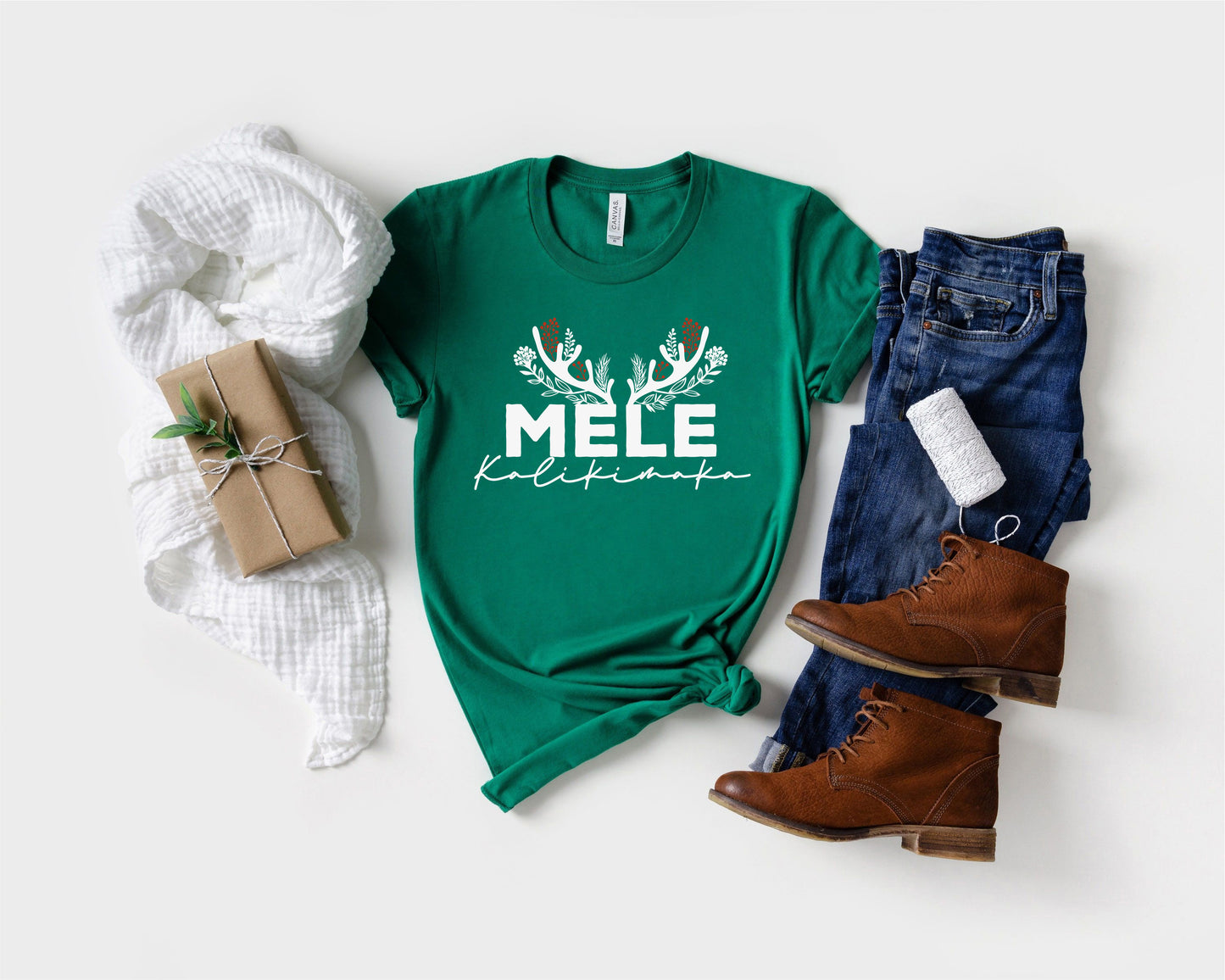 A green t-shirt with the text "MELE" and "Kilimana" printed on it, along with a pair of jeans and brown boots, as well as a wrapped gift and a white scarf.