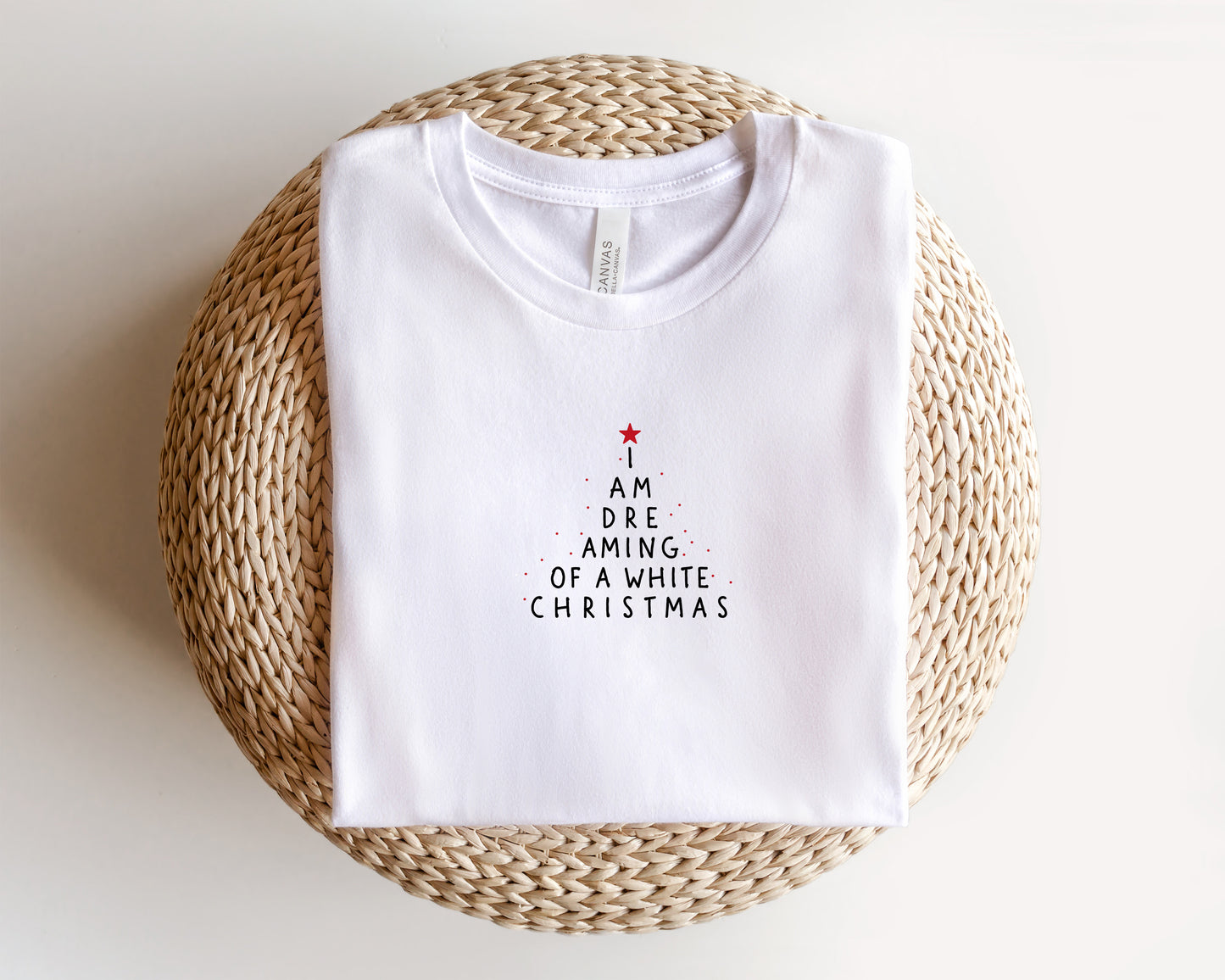 A white t-shirt with a Christmas-themed design printed on it, placed on a woven basket.