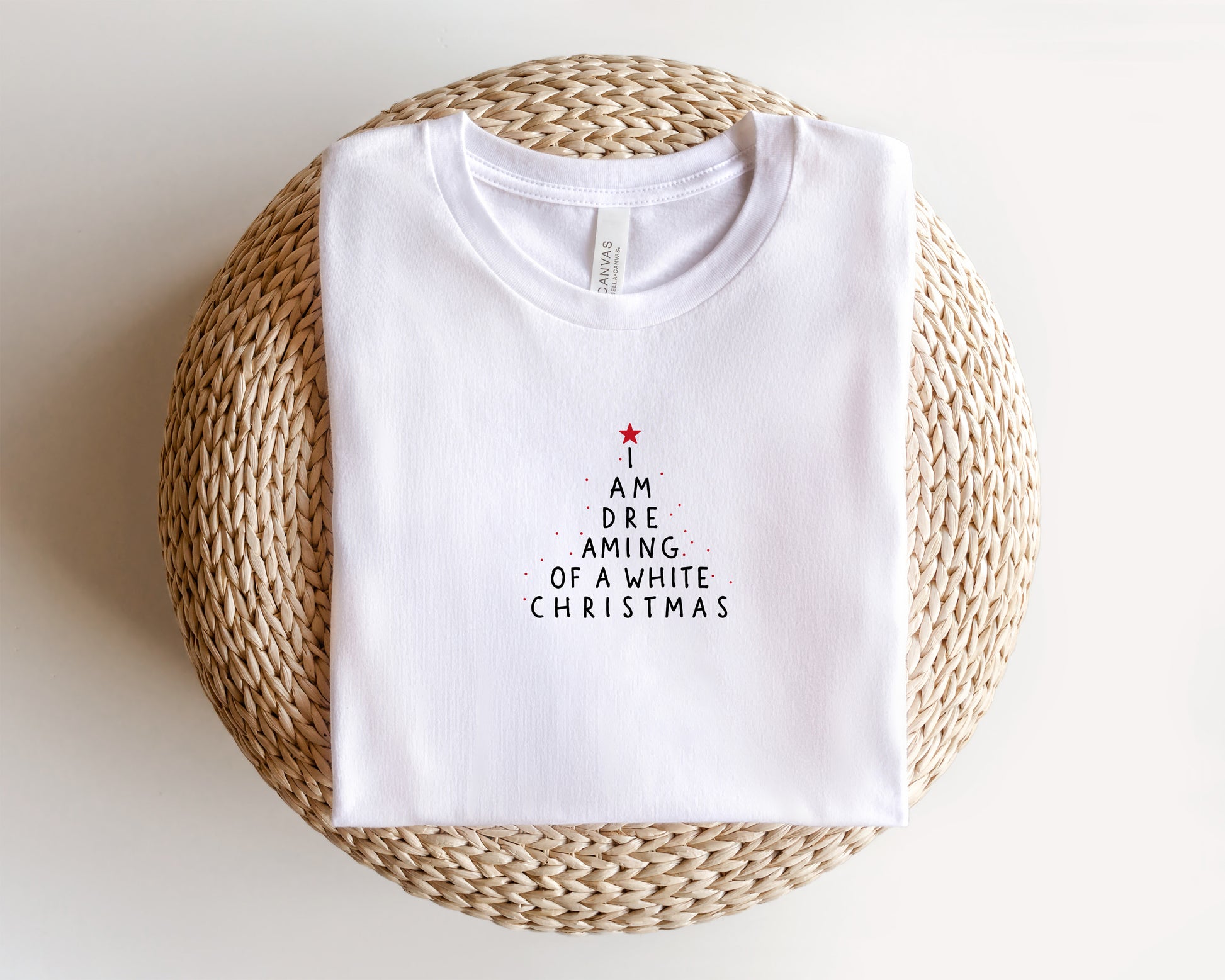 A white t-shirt with a Christmas-themed design printed on it, placed on a woven basket.