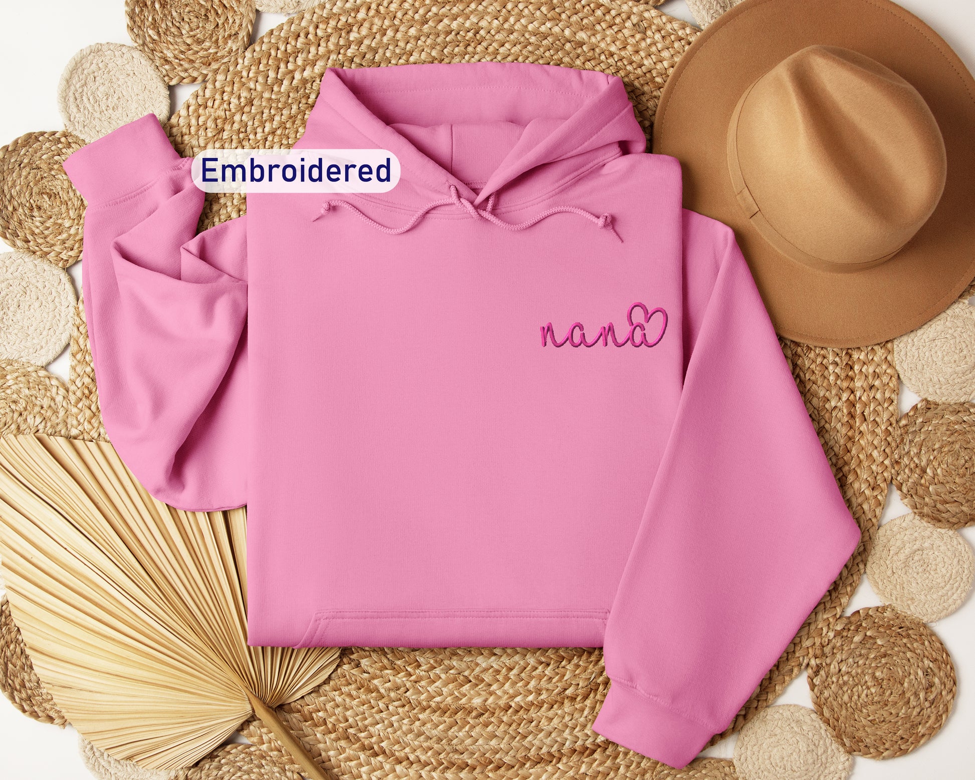 a pink hoodie with embroidered name next to a straw hat