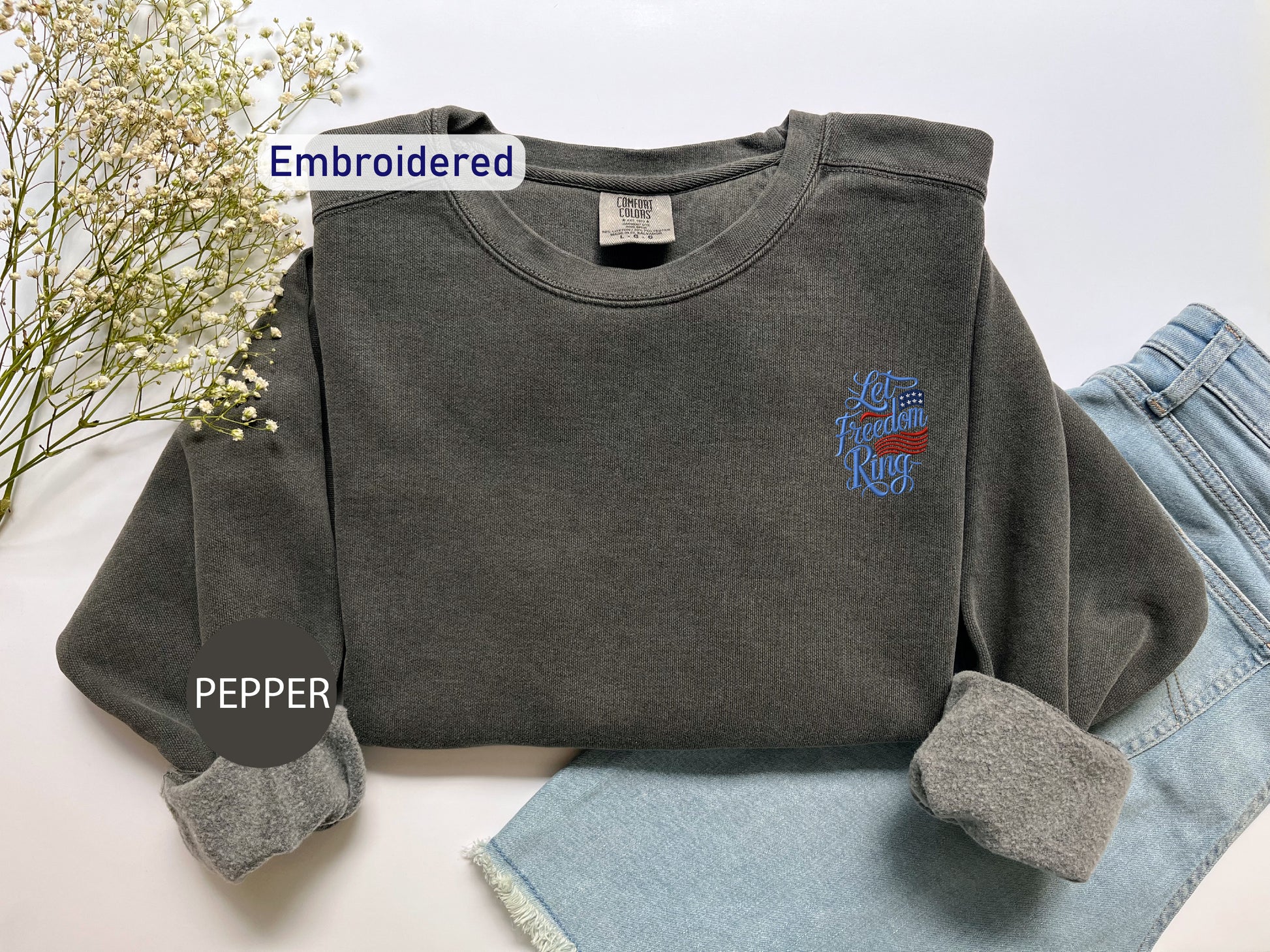 a gray sweatshirt with an embroidered design on the left chest area, placed on top of a pair of blue jeans.