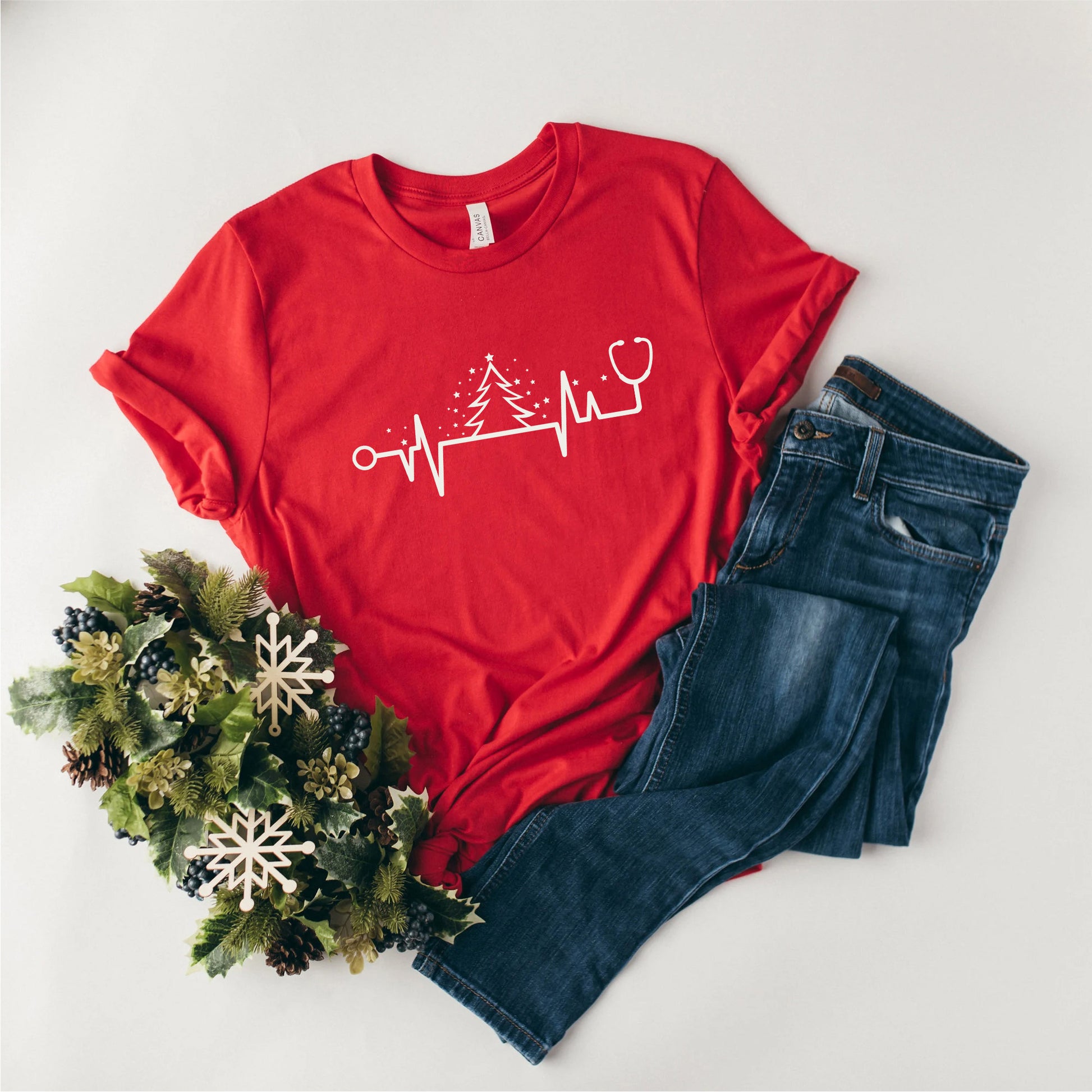 a red t-shirt with a white line drawing of a stethoscope and a tree, along with a pair of blue jeans and a wreath of pine cones.