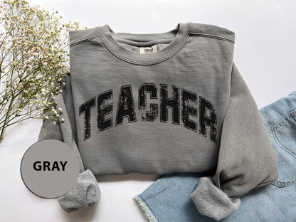 a gray sweatshirt with the word teacher printed on it