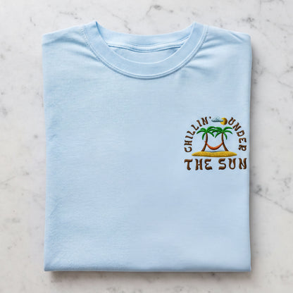 A light blue t-shirt with a graphic design on the front, featuring a palm tree and the text "Chillin' under the sun".