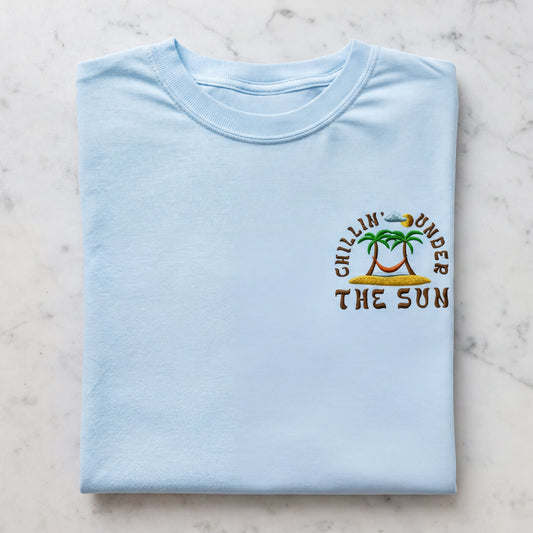 A light blue t-shirt with a graphic design on the front, featuring a palm tree and the text "Chillin' under the sun".